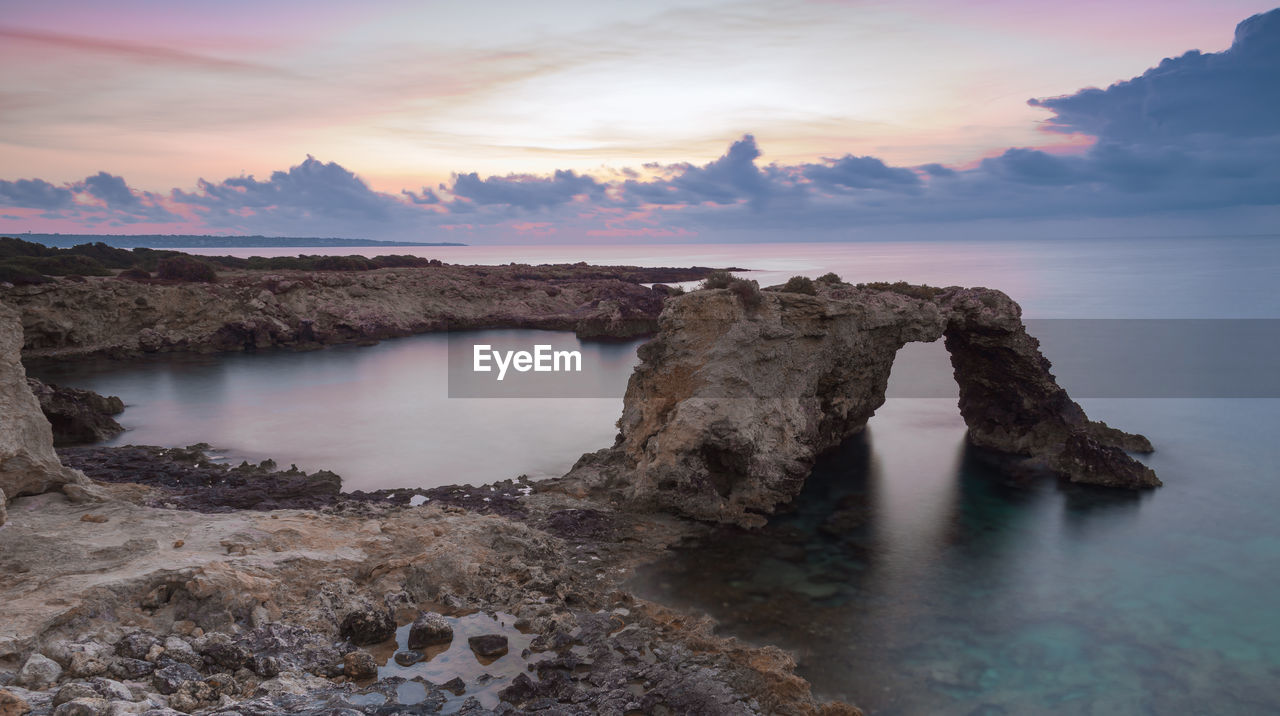 Rocks on sea shore against sky during sunset