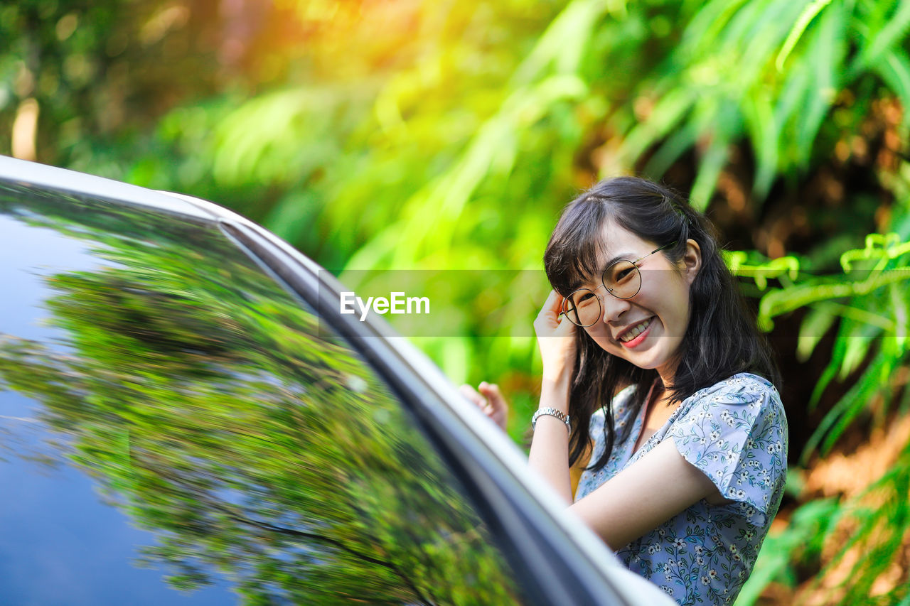 Cheerful young woman standing by car