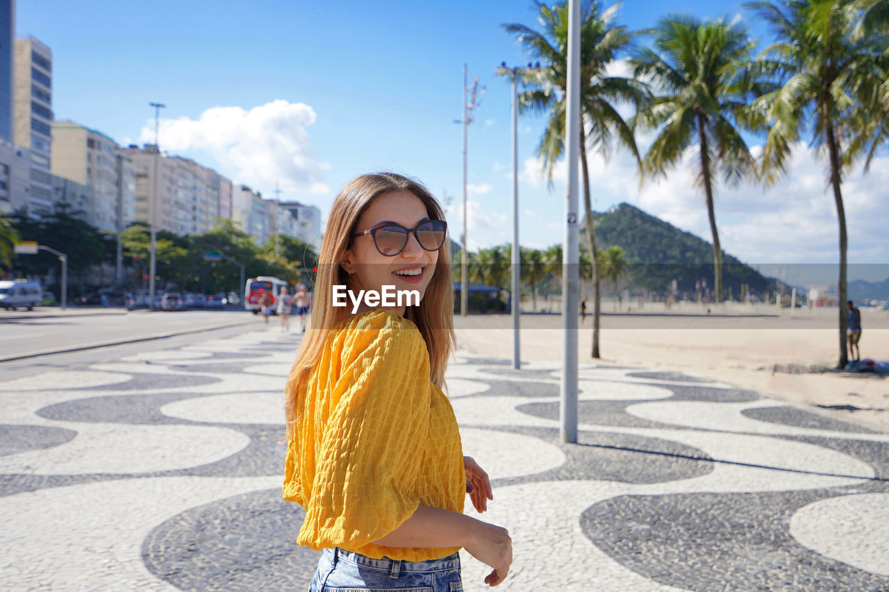 Smiling relaxed traveler woman walking along copacabana beach promenade, rio de janeiro, brazil