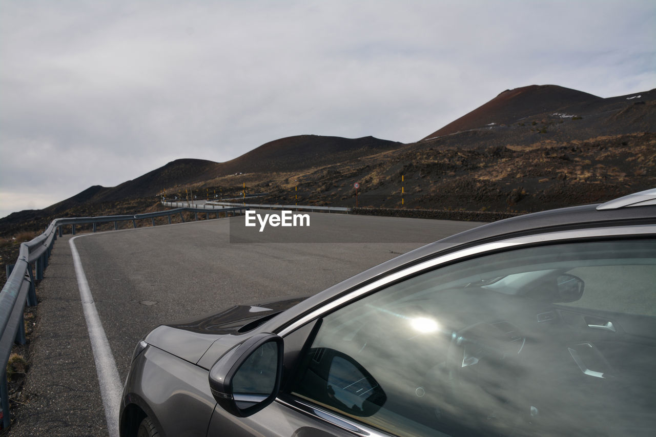 CAR ON ROAD AGAINST MOUNTAIN RANGE