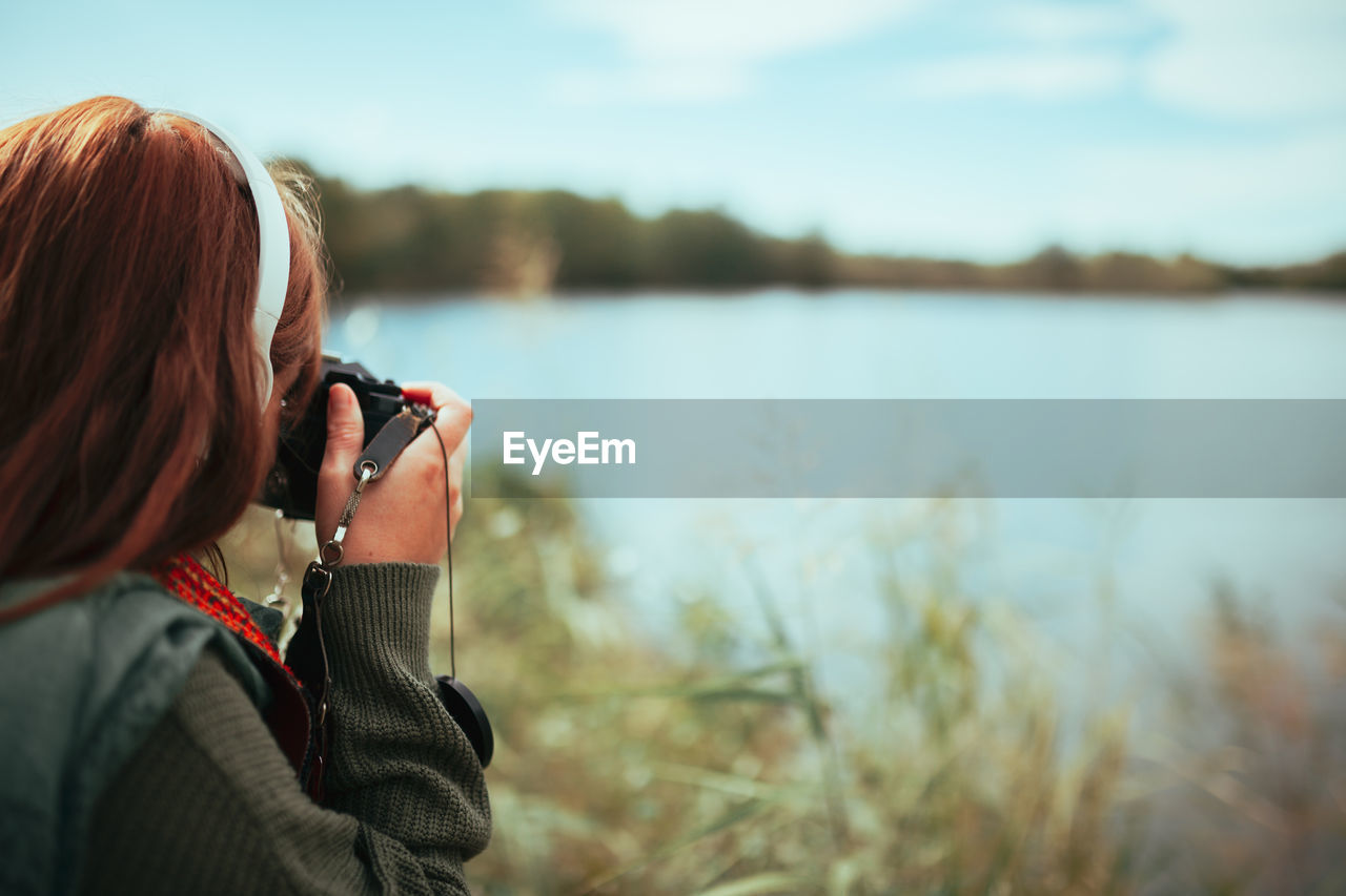 Young woman taking photos near to lake with an old analog camera