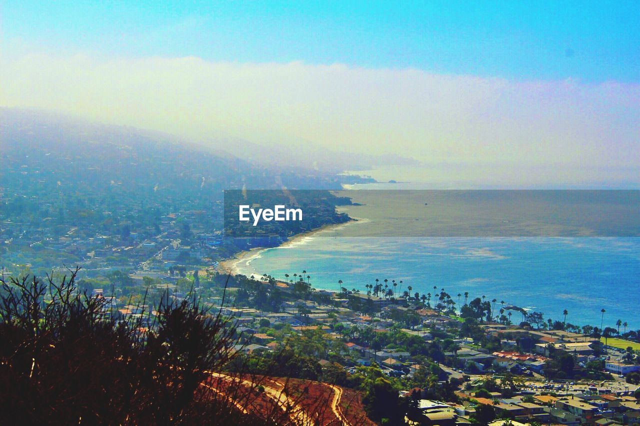 AERIAL VIEW OF SEA BY CITYSCAPE AGAINST SKY