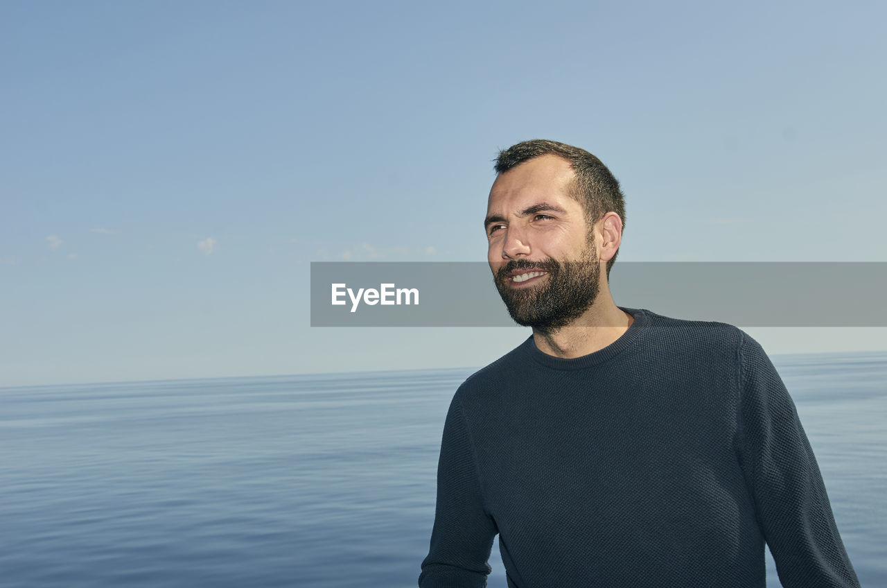 Smiling young man looking away against clear sky