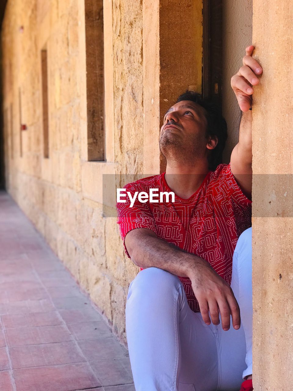 MIDSECTION OF MAN SITTING AGAINST BUILDING