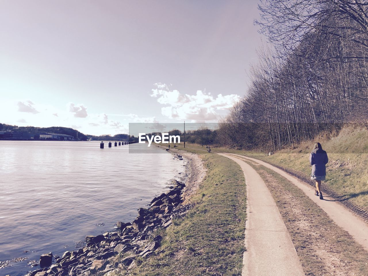 Rear view of woman walking on pathway along calm lake