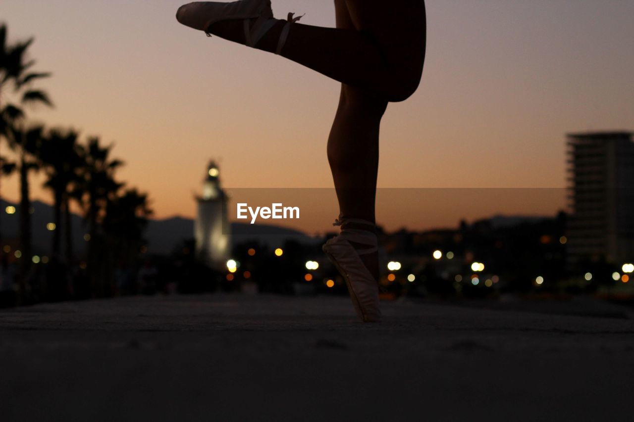 Low section of ballet dancer dancing on road in city