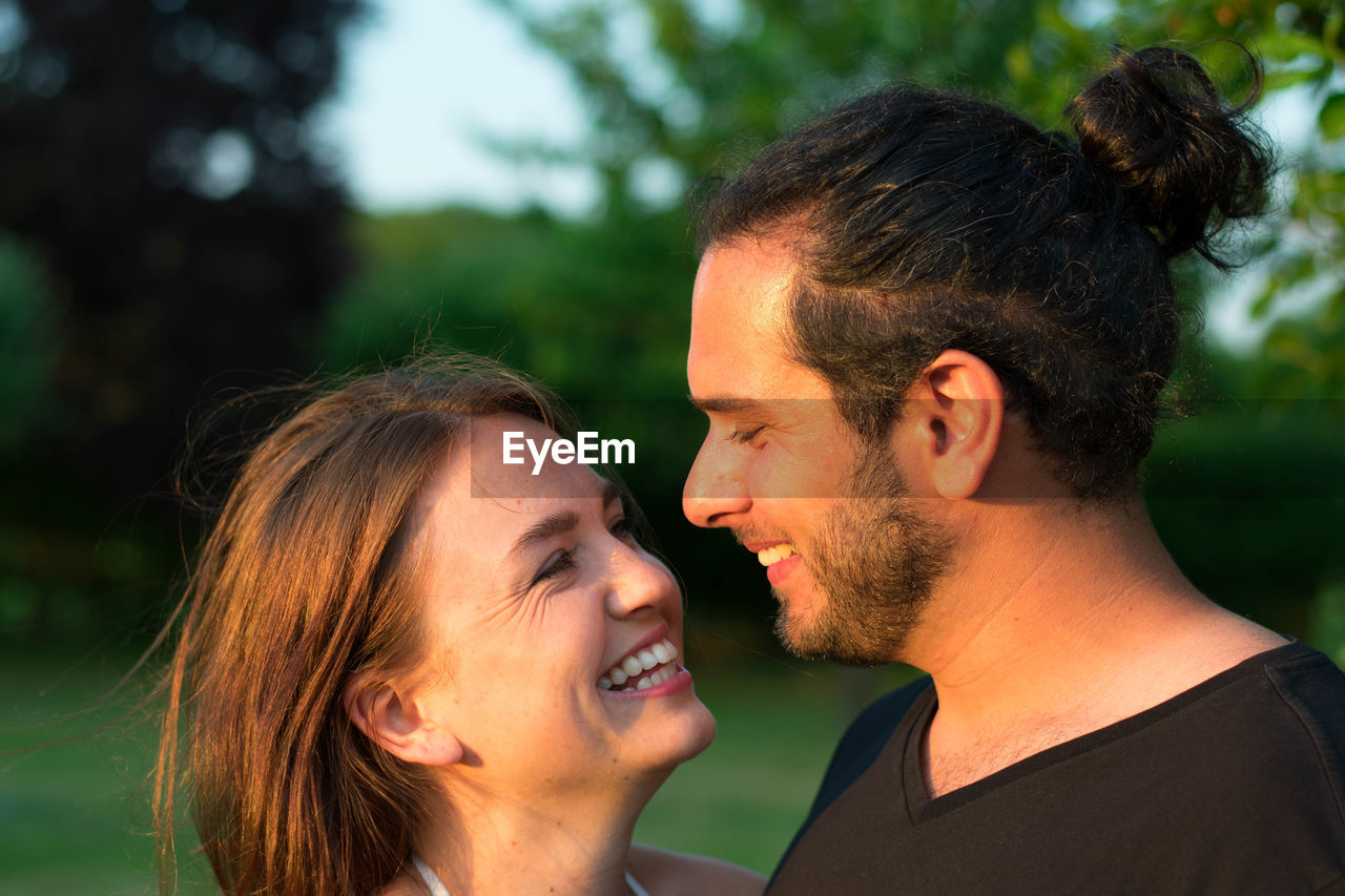 Close-up of smiling young couple against trees