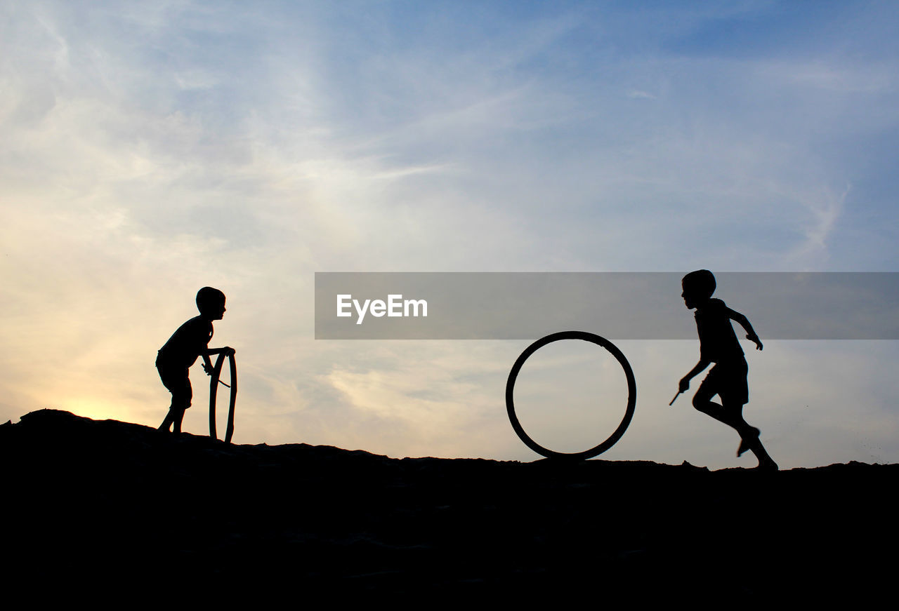 Silhouette boys playing with tires against sky