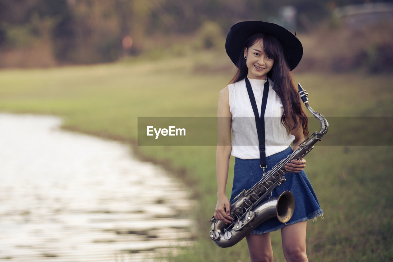 Portrait of smiling woman holding saxophone while standing by lake