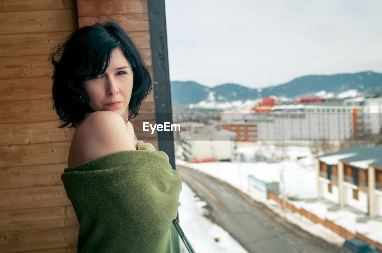 Portrait of topless woman with blanket standing in balcony