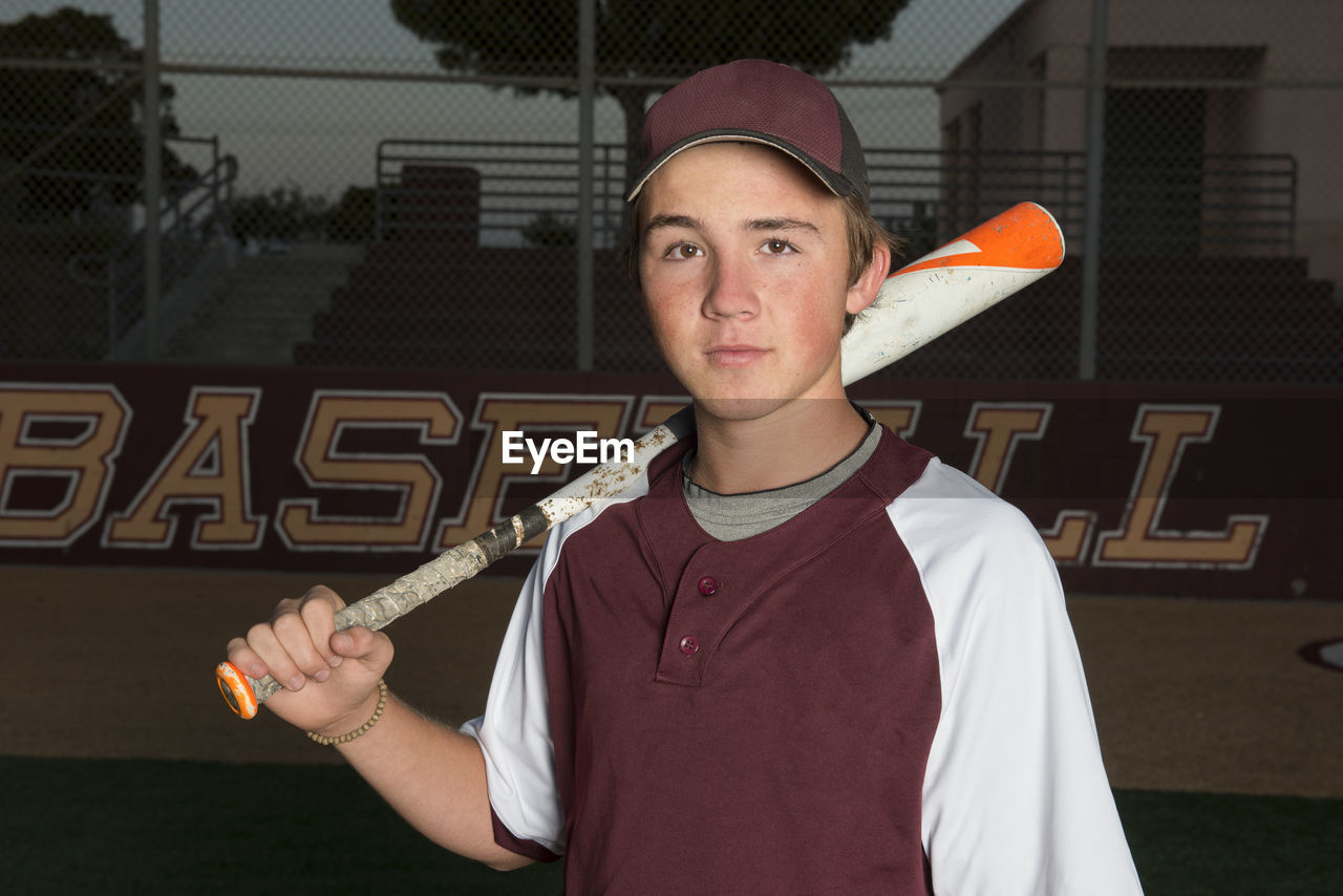 Portrait of a high school baseball player in maroon uniform holding his bat