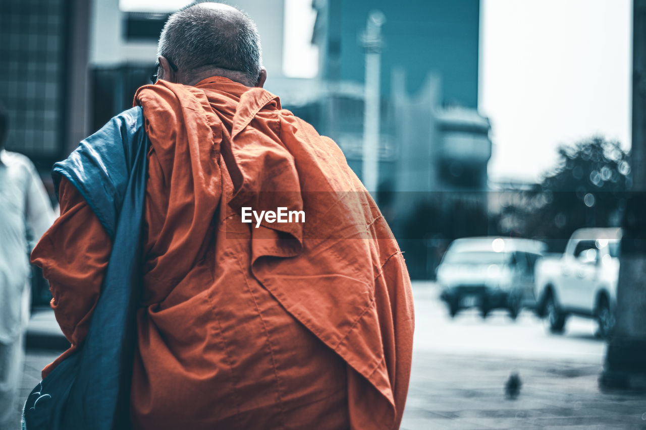 Rear view of monk walking on road in city