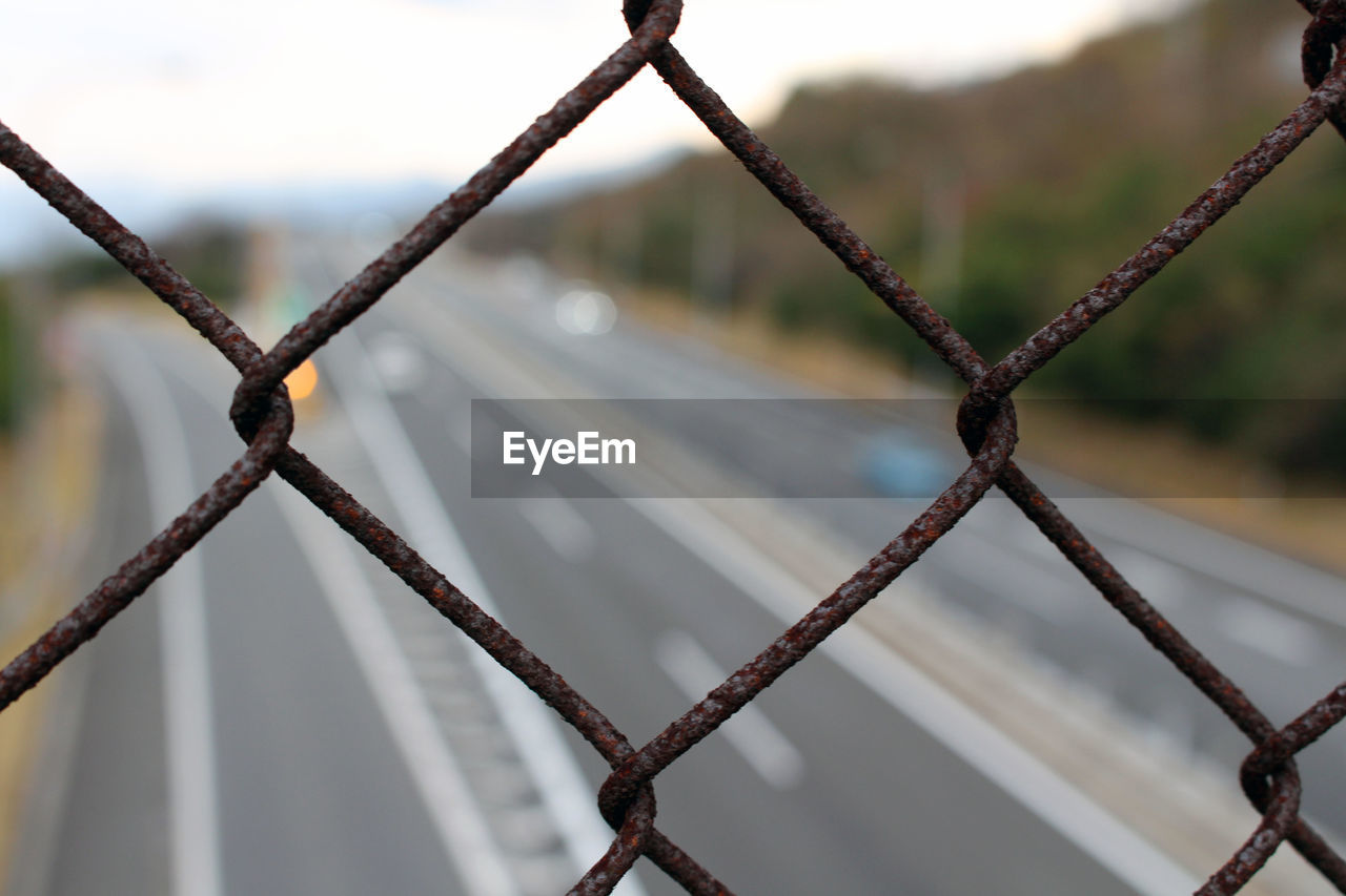 CLOSE-UP OF CHAINLINK FENCE AGAINST BLURRED BACKGROUND AGAINST SKY