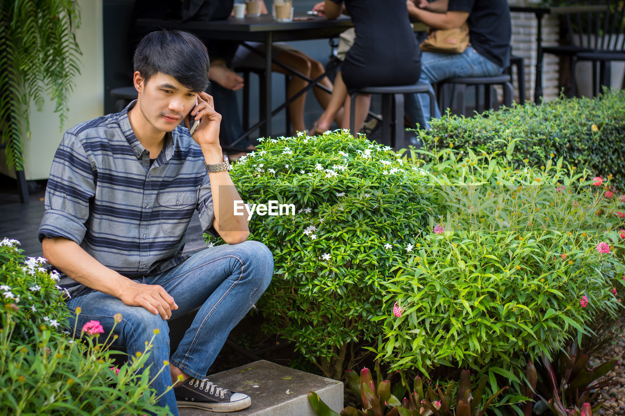 Young man talking on phone while sitting on steps amidst plants