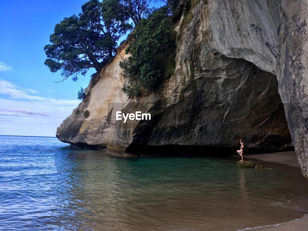 Woman practicing yoga on rock in cave by sea against sky