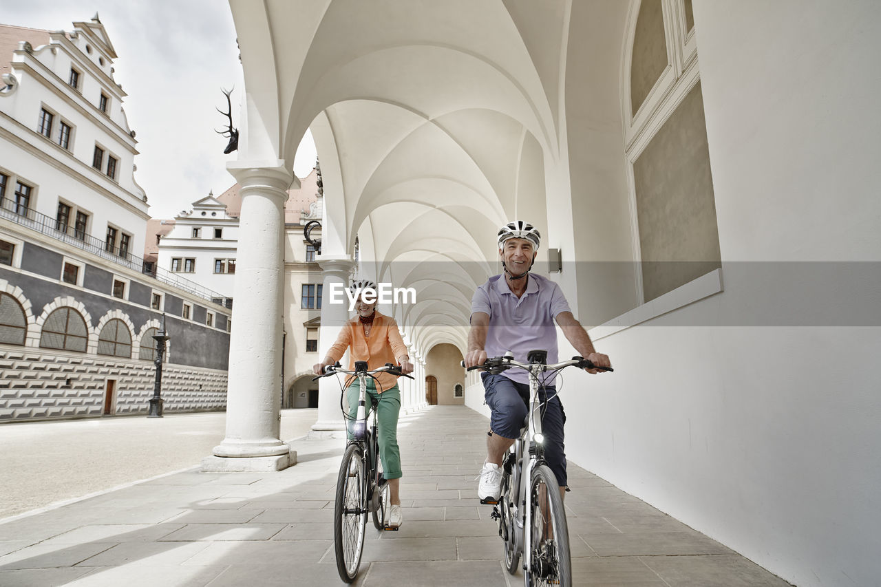 Smiling senior couple riding electric bicycle on footpath at dresden, germany