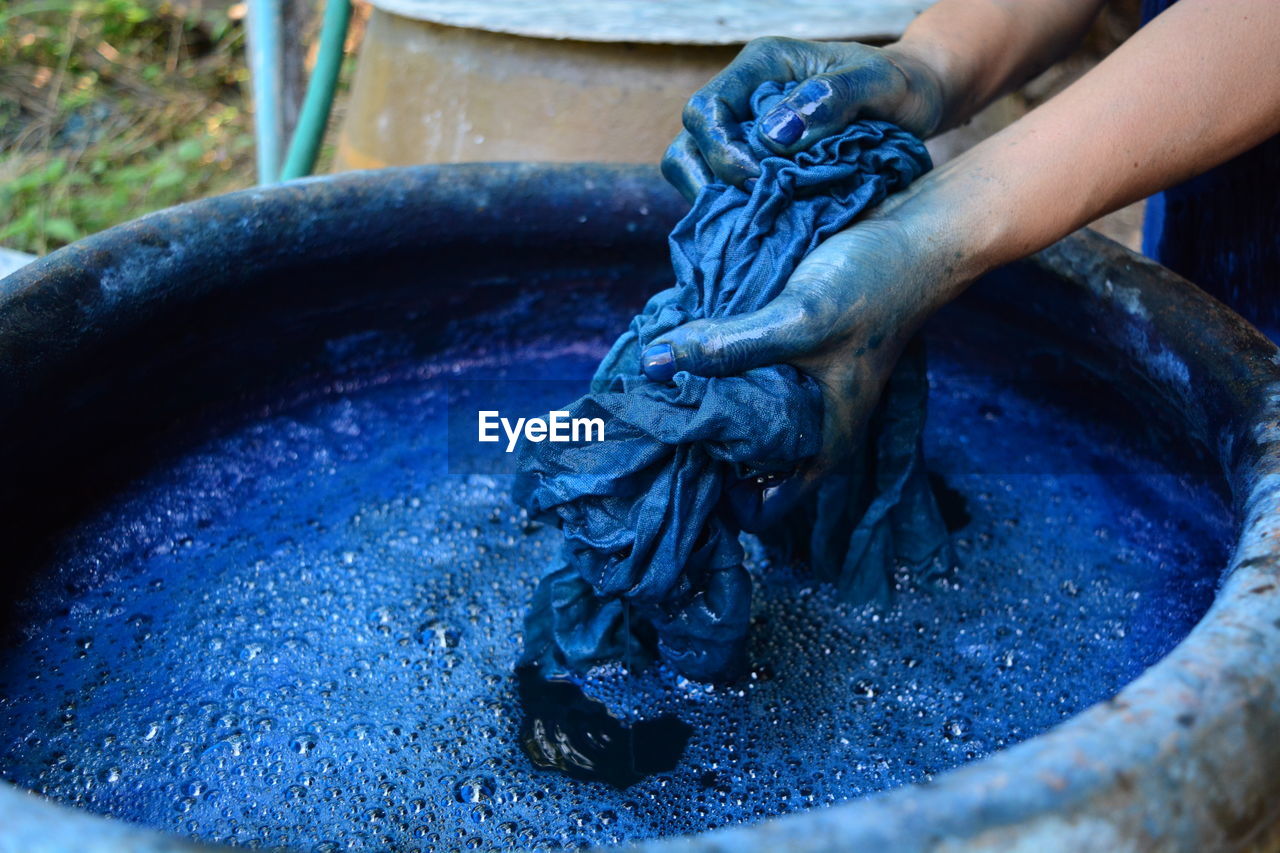 Cropped hands of woman washing textile in blue water