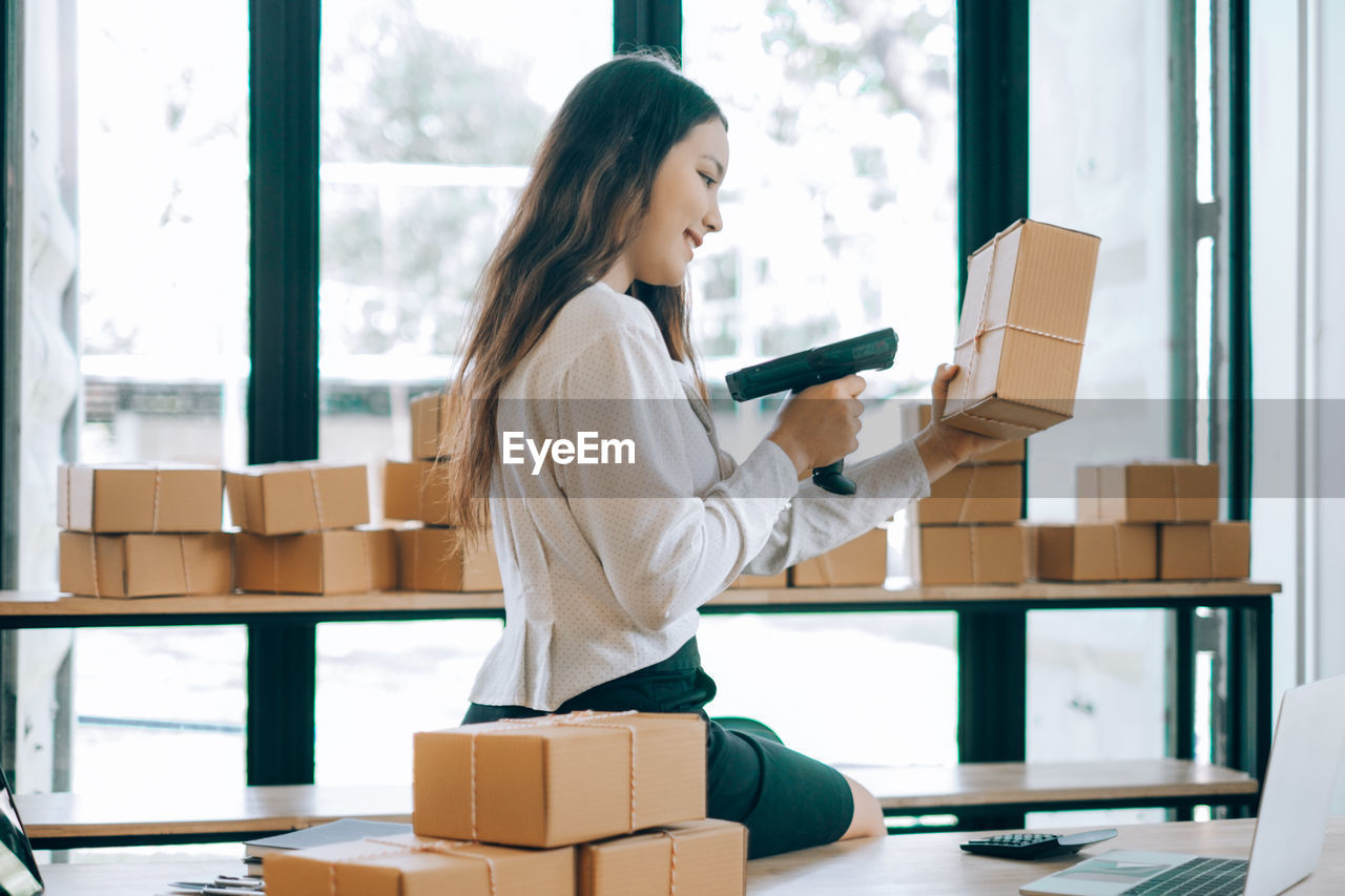 Young businesswoman working while sitting by packages at office