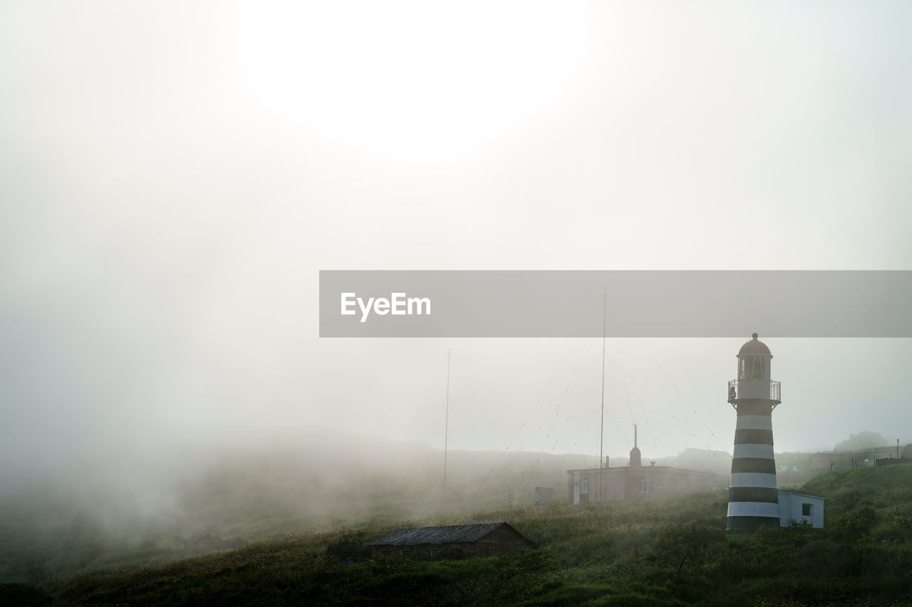 Lighthouse on landscape against sky during foggy weather