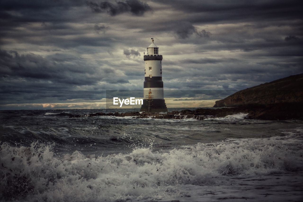 LIGHTHOUSE BY SEA AGAINST BUILDINGS AND SKY