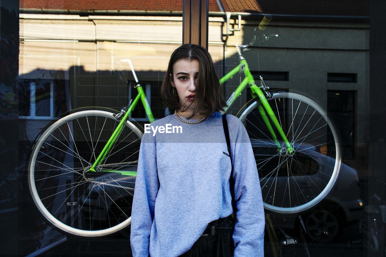 PORTRAIT OF SMILING WOMAN WITH BICYCLE STANDING AGAINST IN SUNLIGHT