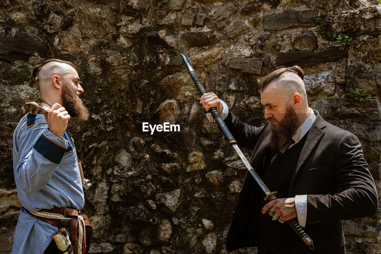 Man looking at businessman holding sword against rock formation