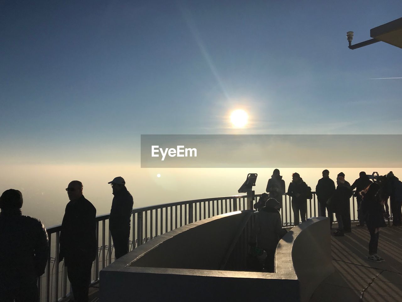 PEOPLE STANDING ON RAILING AGAINST SEA DURING SUNSET