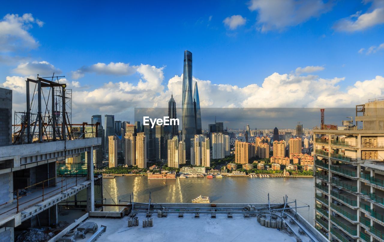 High angle view of cityscape by river against cloudy sky