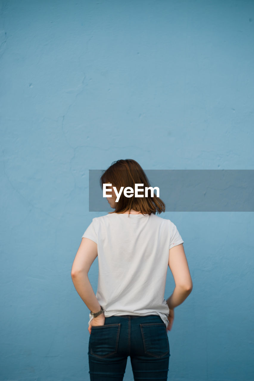 Rear view of young woman standing against blue wall