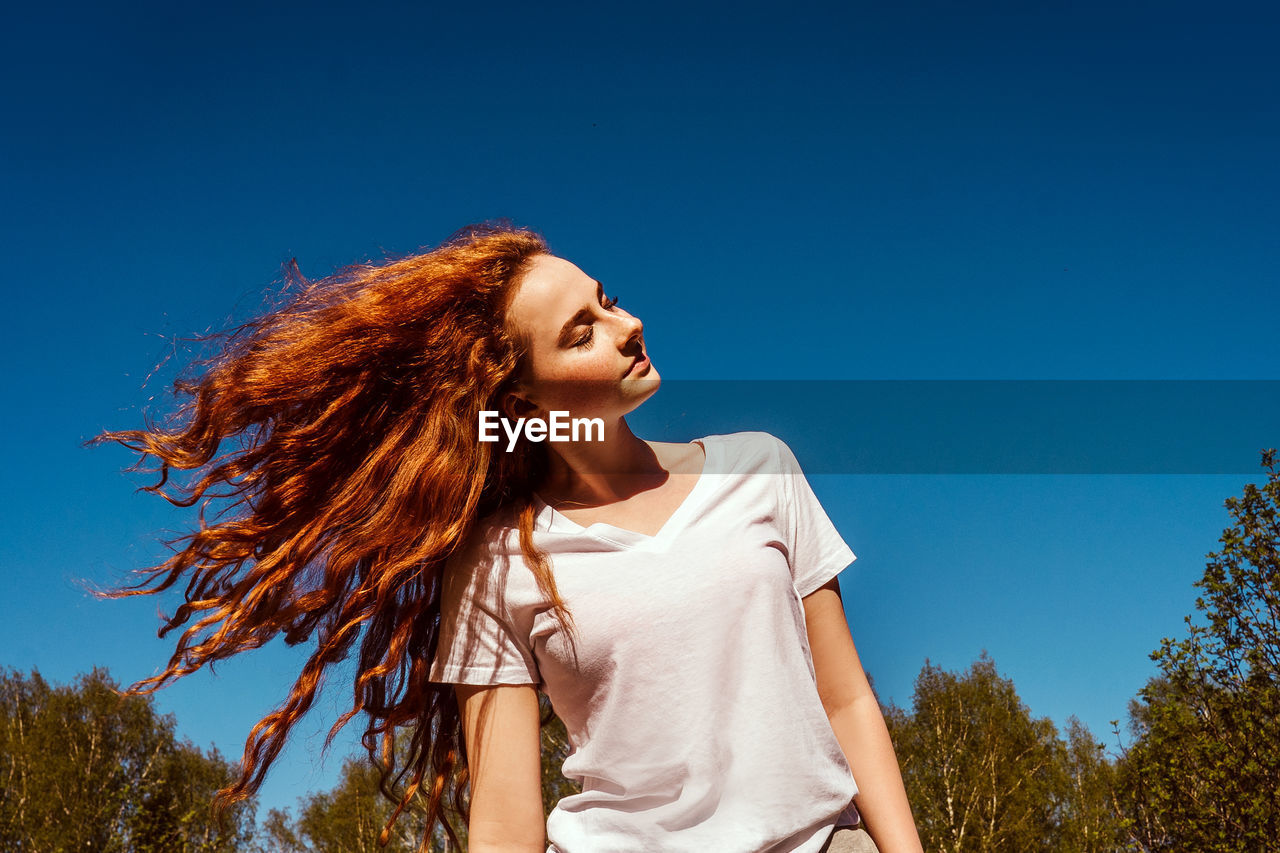 Low angle view of girl tossing hair against sky