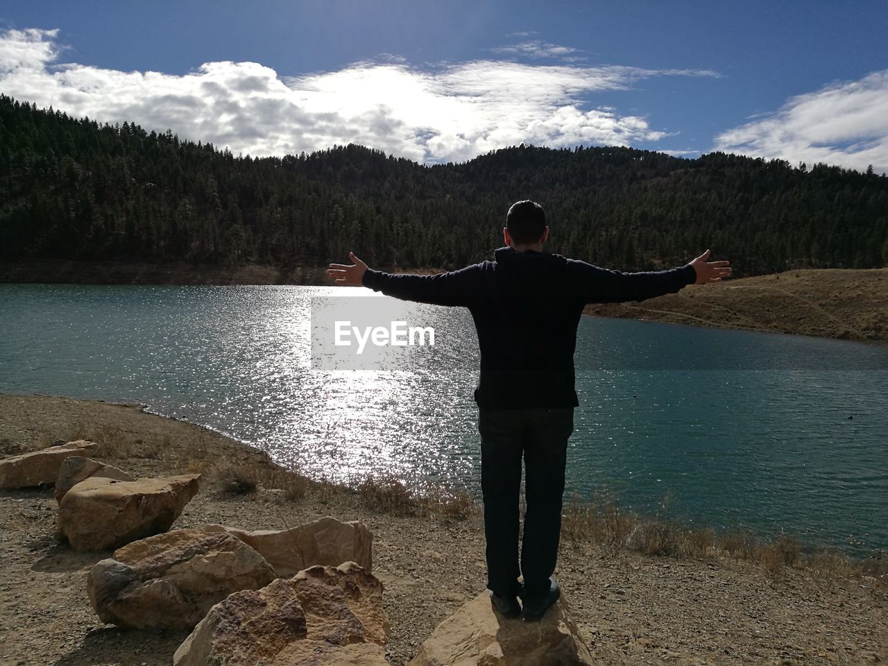 Rear view of man standing at lake against sky