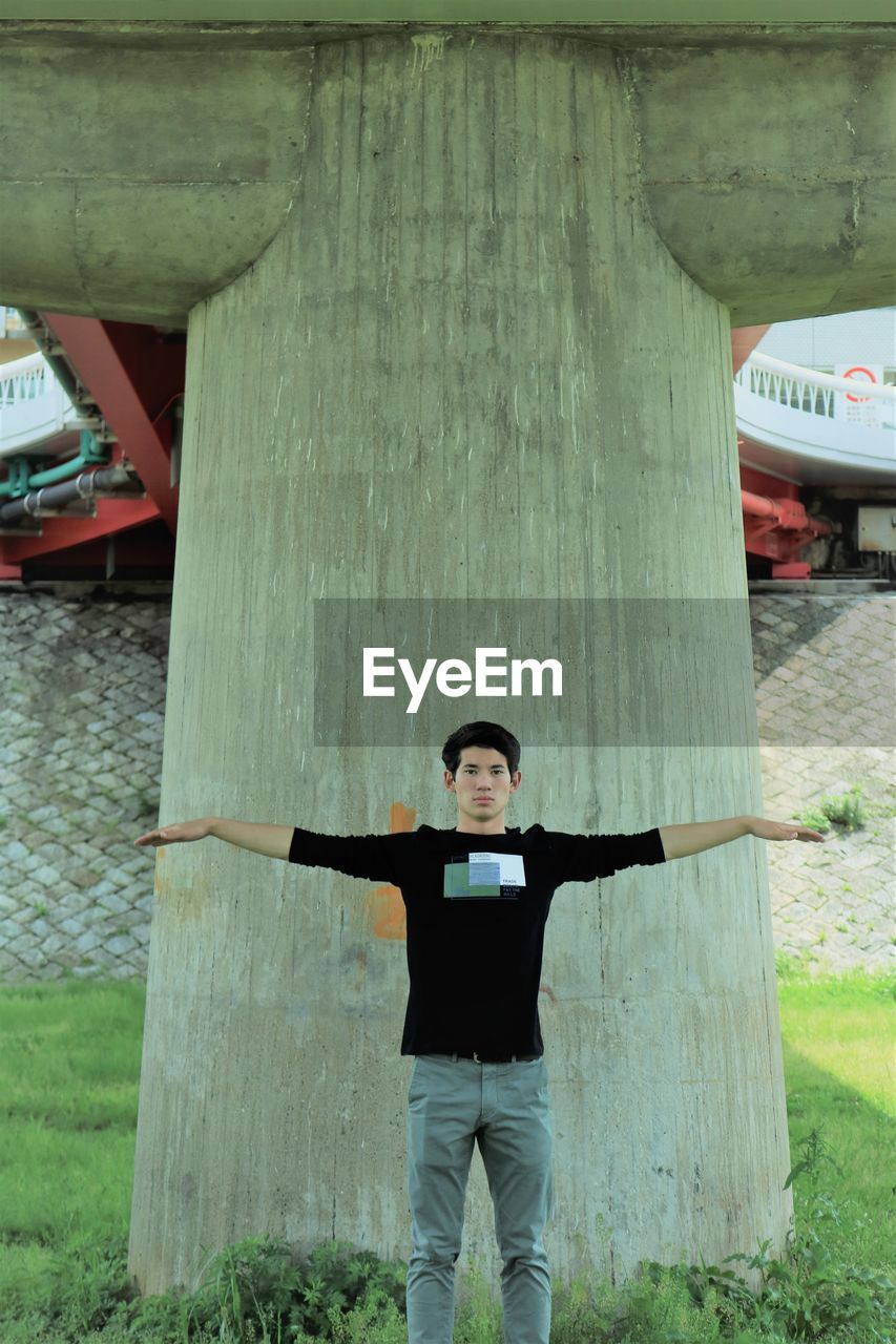 FULL LENGTH PORTRAIT OF YOUNG MAN STANDING ON WOODEN WALL