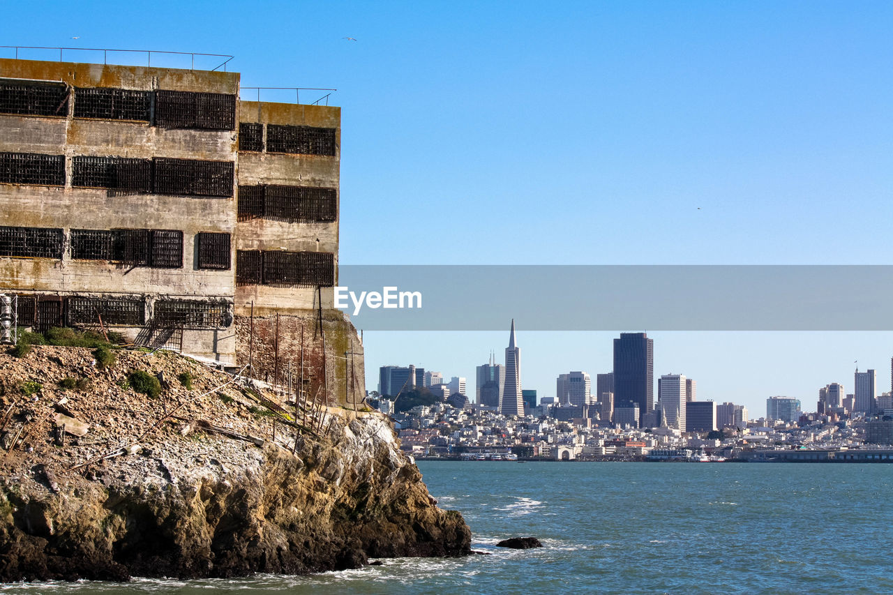 View of city at waterfront against blue sky