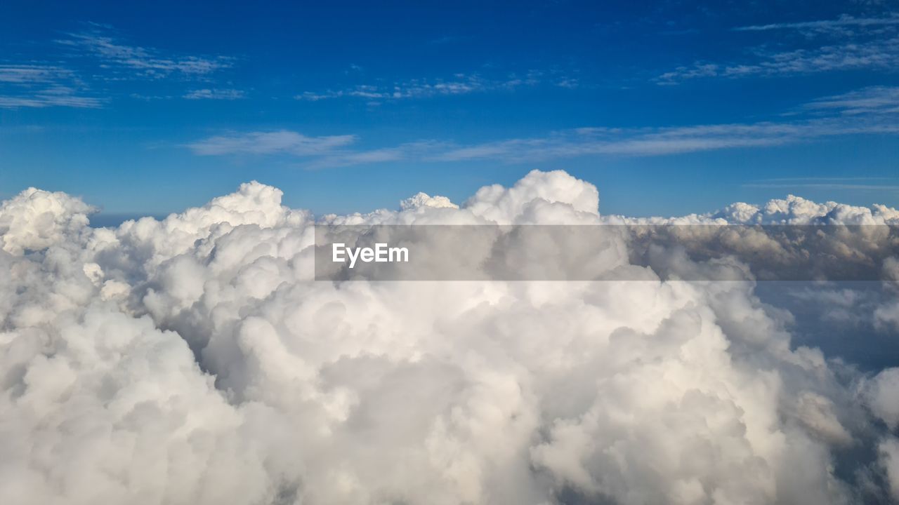 sky, cloud, cloudscape, daytime, blue, environment, nature, beauty in nature, airplane, atmosphere, high up, fluffy, scenics - nature, white, outdoors, no people, backgrounds, travel, dramatic sky, aerial view, idyllic, landscape, wind, flying, day, storm cloud, overcast, cumulonimbus, softness, sunlight, summer, animal wing, tranquility, above, air vehicle, journey, fly