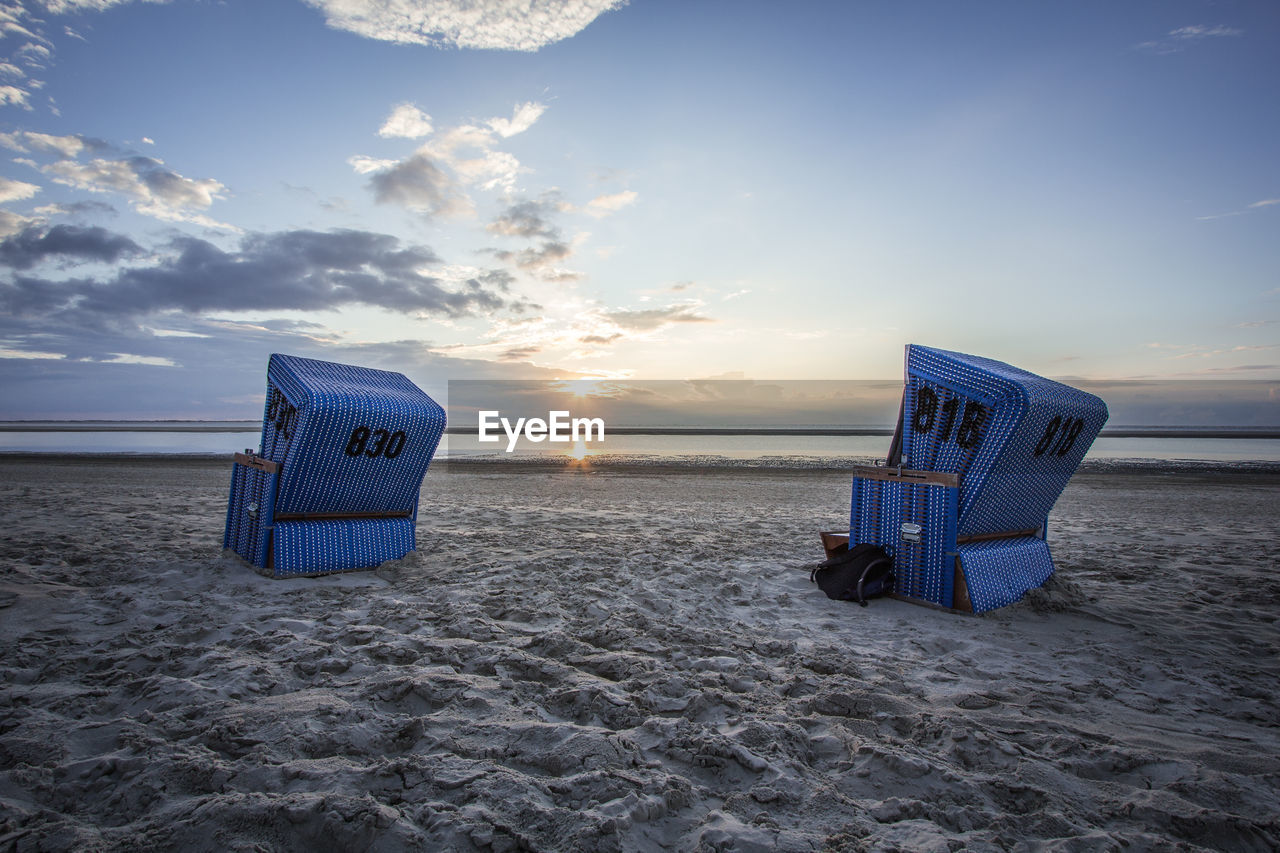 Hooded chairs at beach against sky during sunset