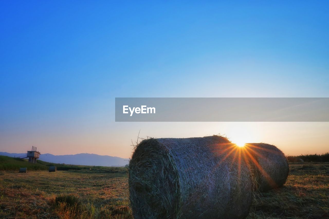 Hay bales on field against clear sky at sunset