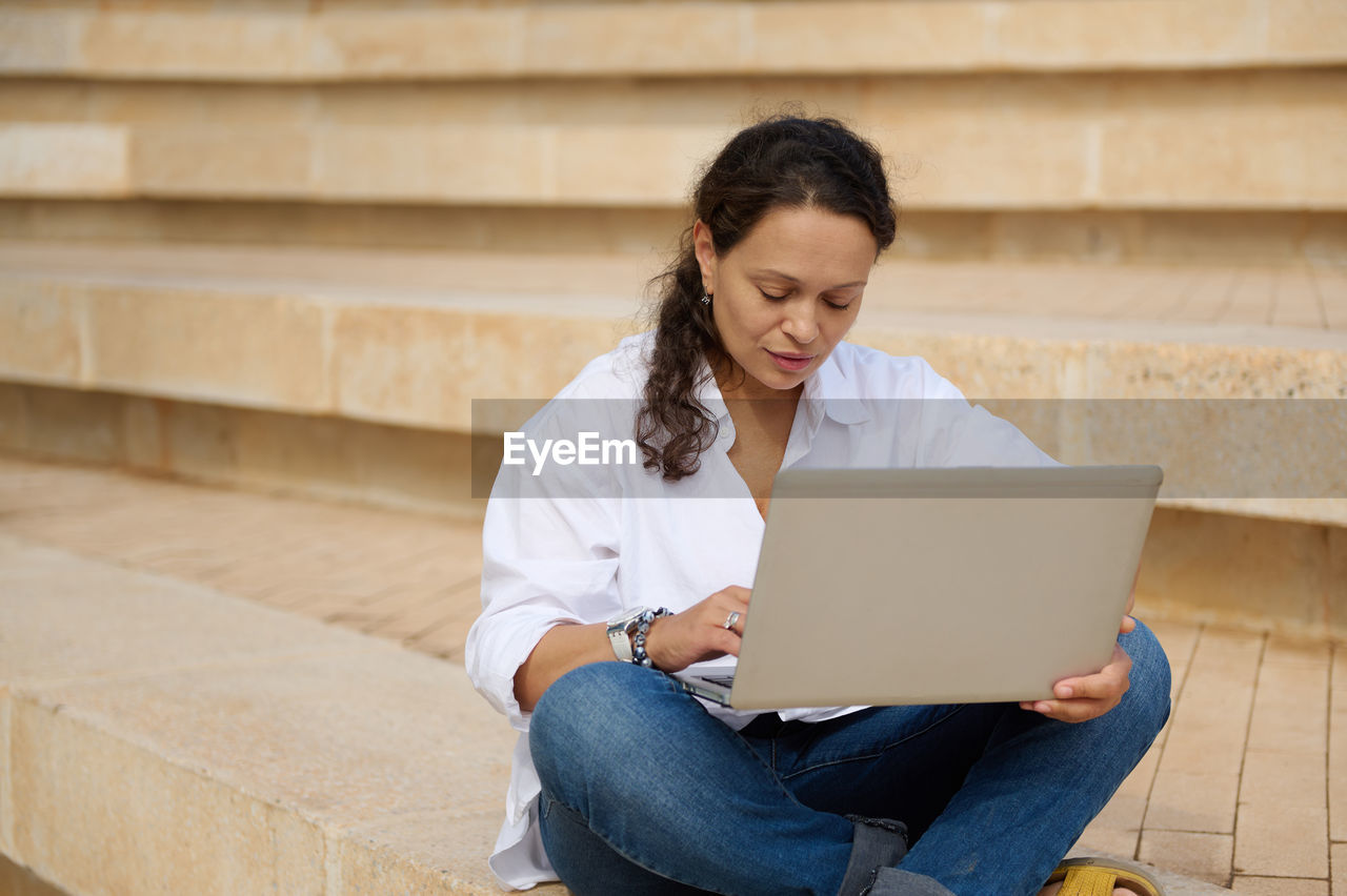 young woman using laptop while sitting on staircase