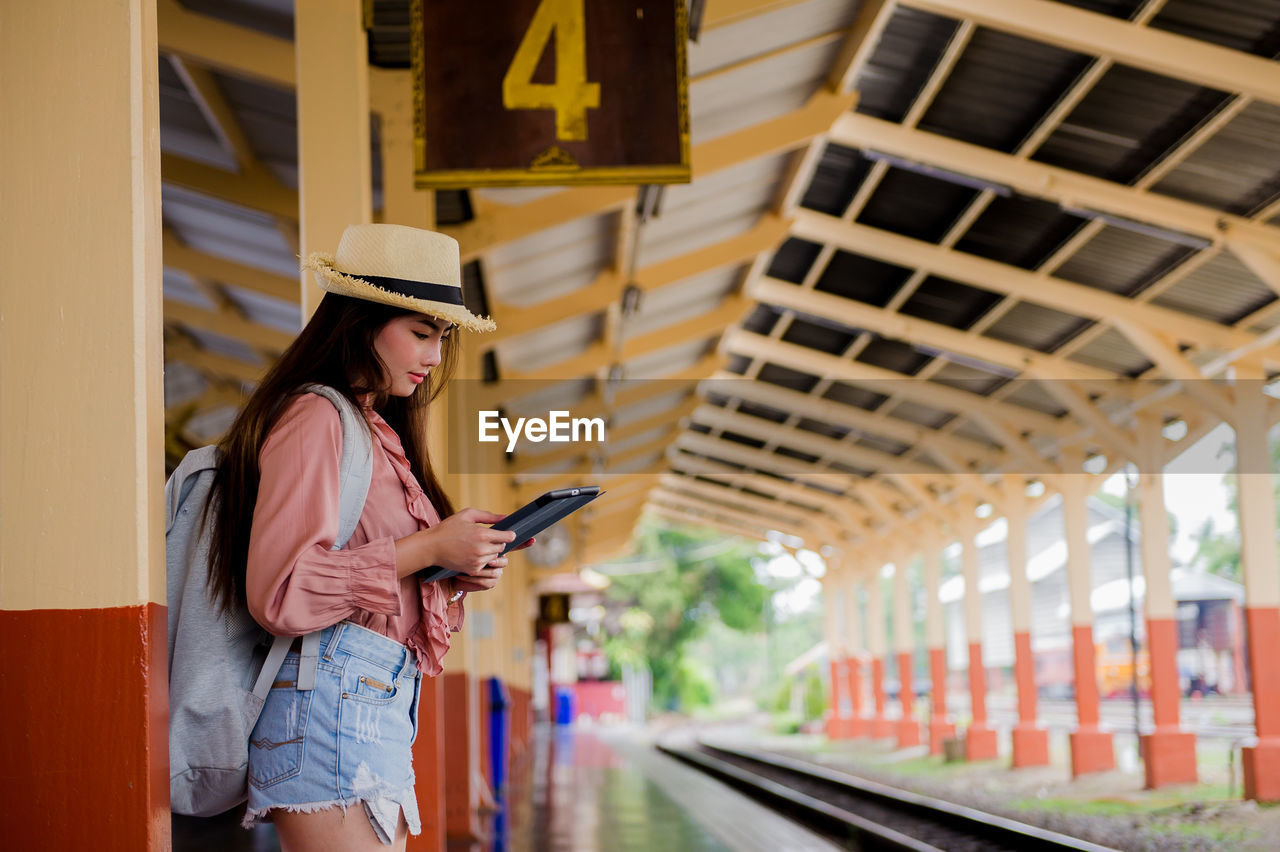 Woman using digital tablet while standing at railroad station platform