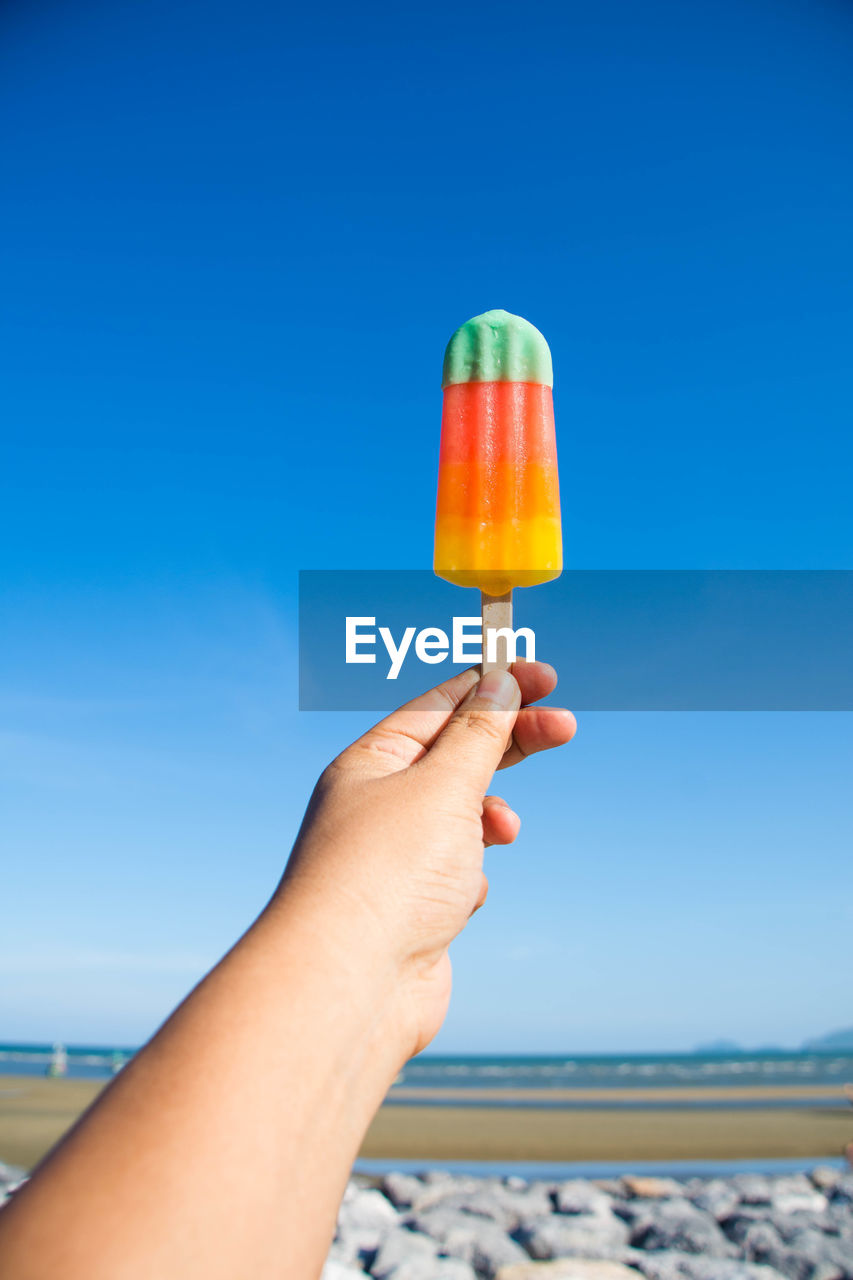 Cropped image of person holding flavored ice cream against sky