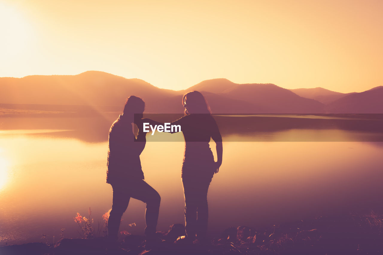 Silhouette couple standing on mountain against sky during sunset