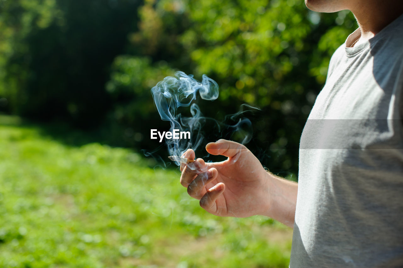 Midsection of woman holding burning cigarette against trees