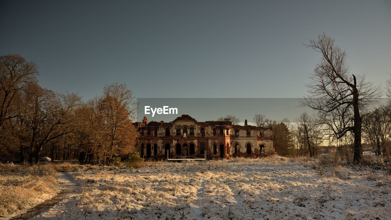 ABANDONED BUILDING BY TREES ON FIELD AGAINST SKY