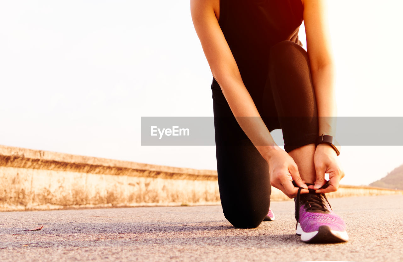 Low section of woman tying shoelace while kneeling on road