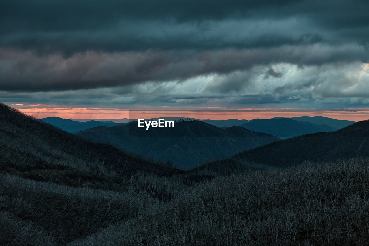 Scenic view of mountains against cloudy sky during sunset