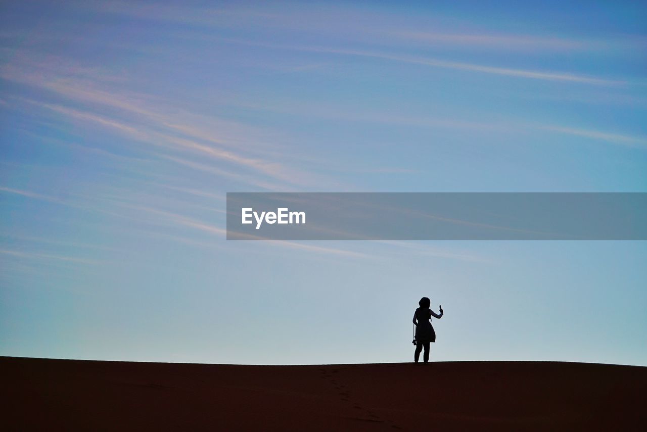 Silhouette woman in sahara desert against clear sky