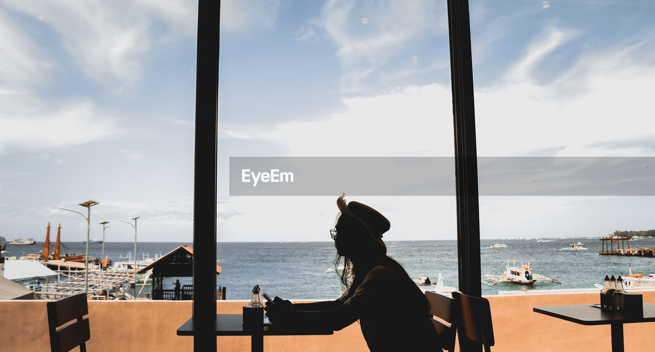 Man sitting on table in restaurant by sea against sky