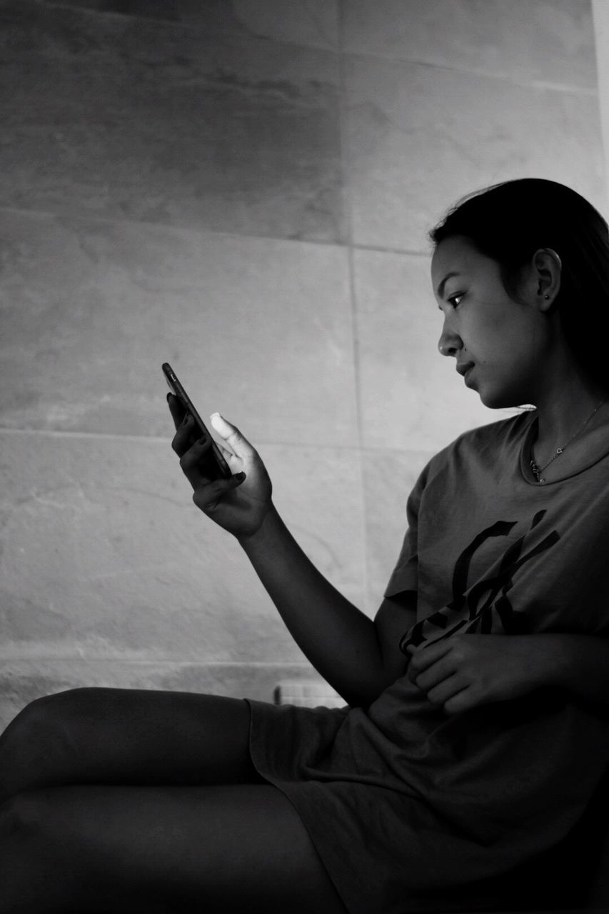 Woman using smart phone while sitting against wall