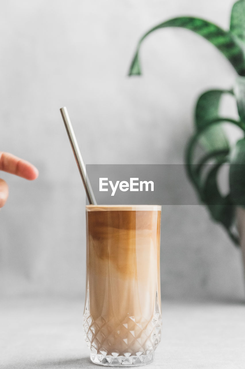 Close-up of female reaching out for metal straw in iced coffee cup on table