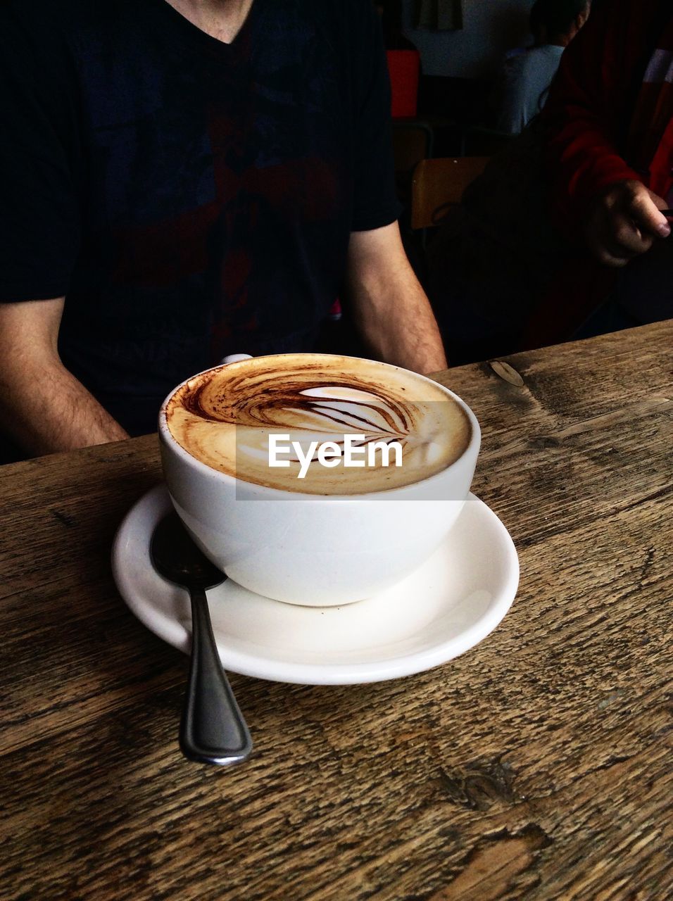 Midsection of man sitting by coffee cup on table at cafe