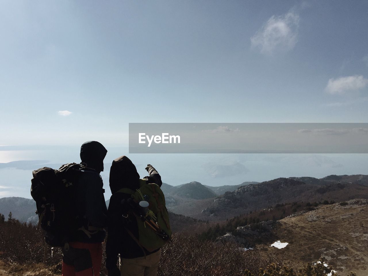 Rear view of hikers standing on mountain against sky